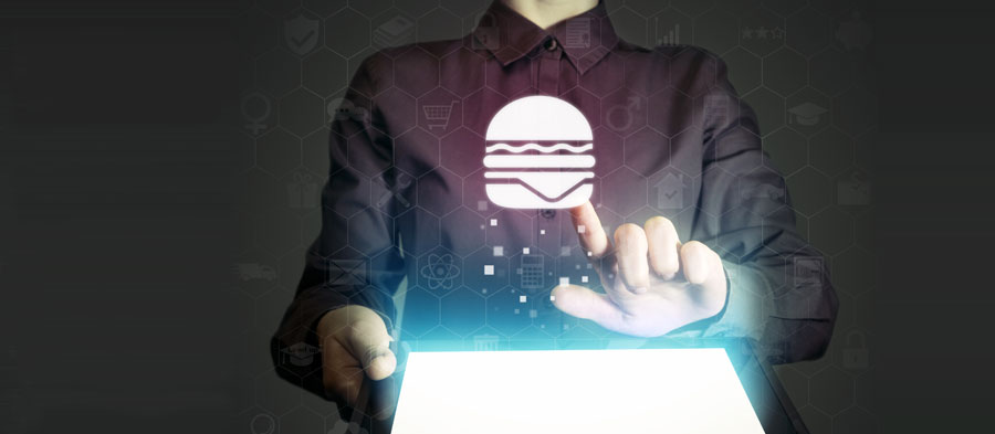 A person off-screen uses a smart tablet and reaches out to tap an icon of a hamburger.