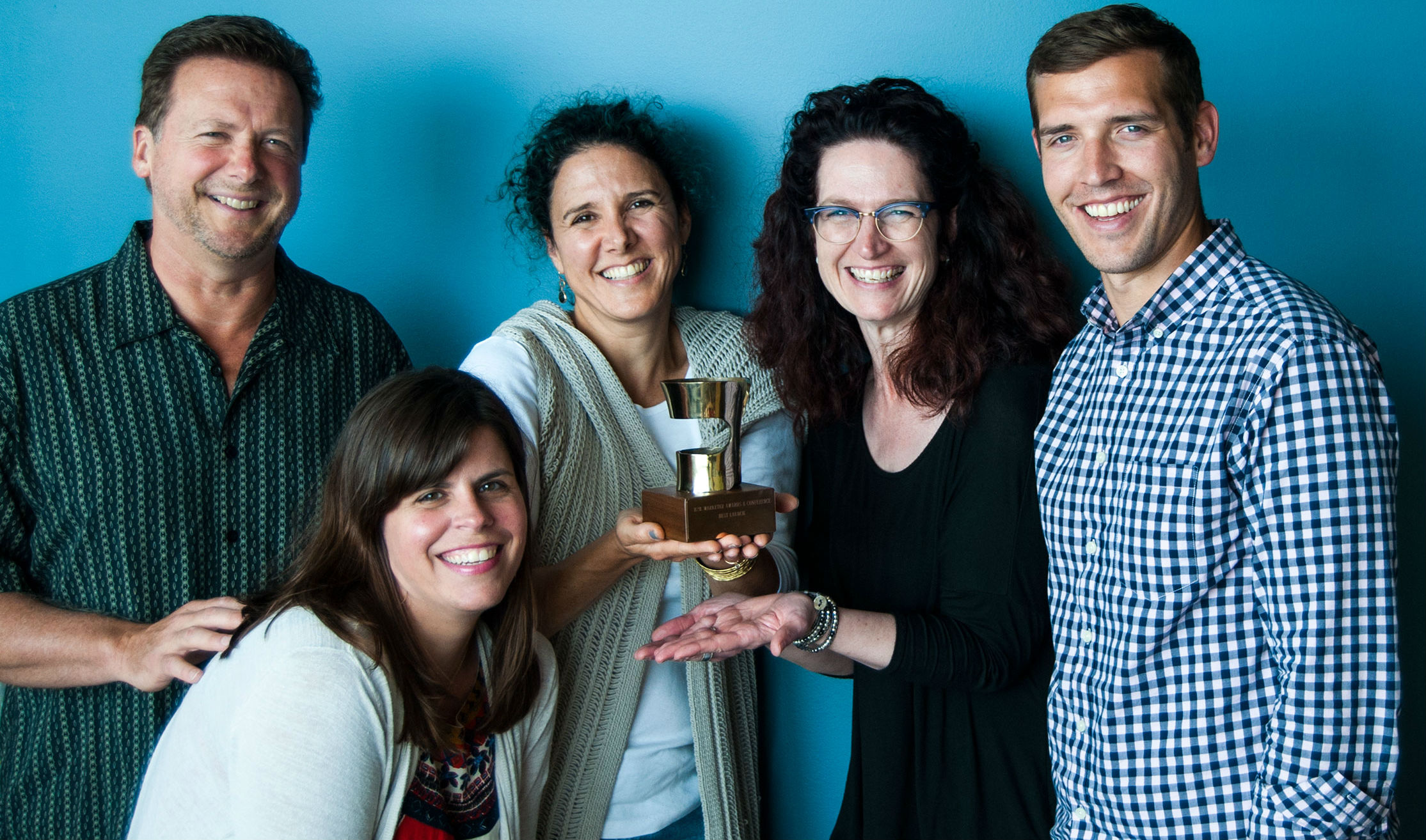 Several people in business-casual clothing hold and award together and smile towards the camera.