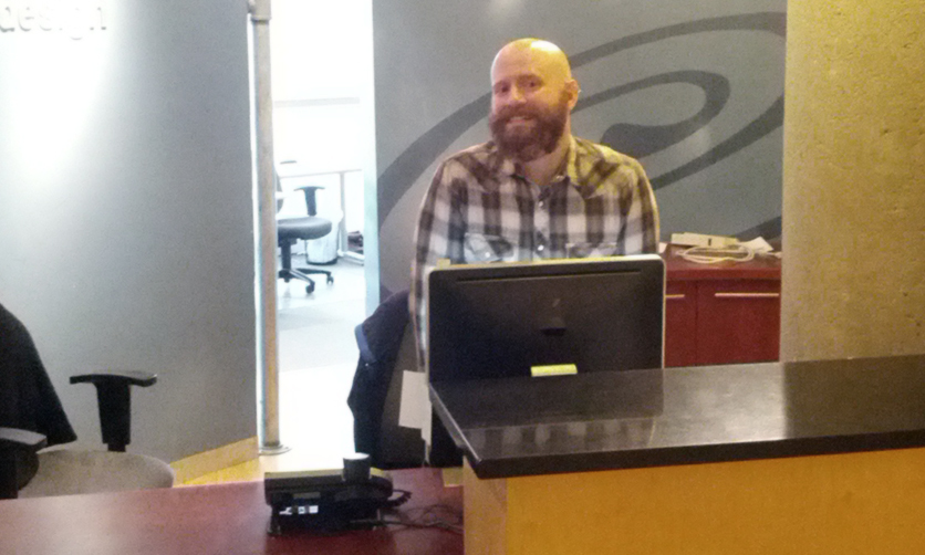 Sandstormer smiles behind reception desk at Sandstorm office.