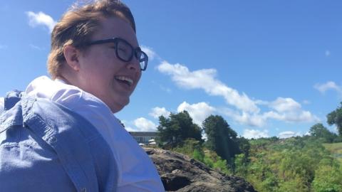 A light-skinned non-binary person wearing black glasses and a white shirt smiles wide.